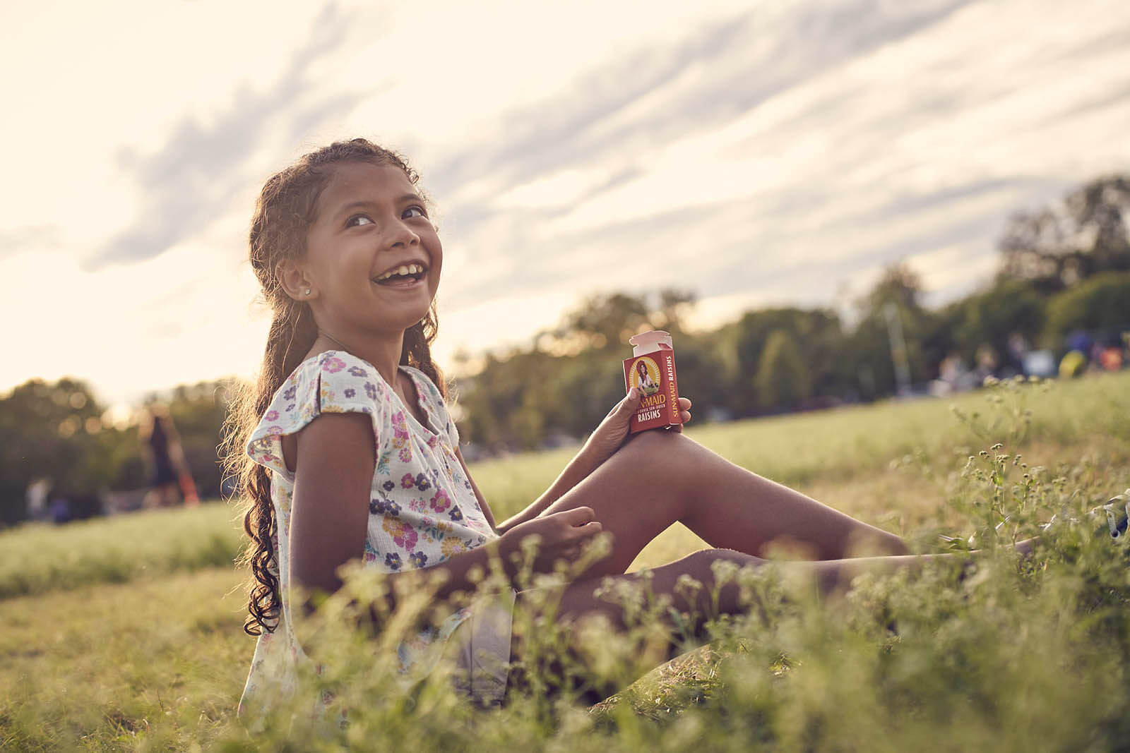 Child sitting in a field eating Sun-Maid raisins